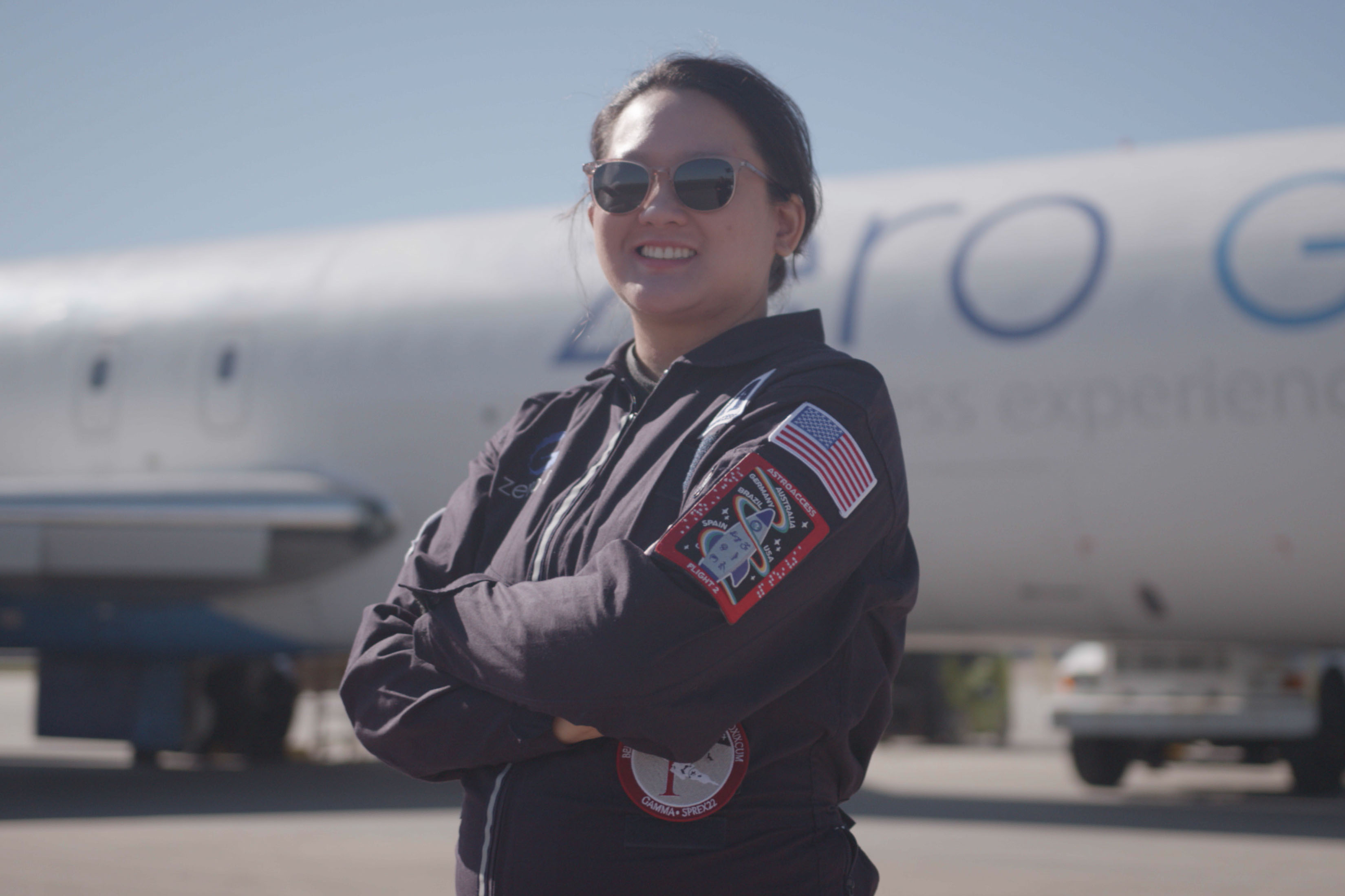 A photo of Sheila Xu standing on a tarmac in front of a plane 