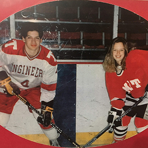 A photo of MIT alums Josh Fedderly and Wendy Fedderly standing in a hockey rink with hockey equipment on and sticks