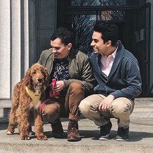 A photo of Anthony Martorell and Francisco Peña bending down with a dog next to them