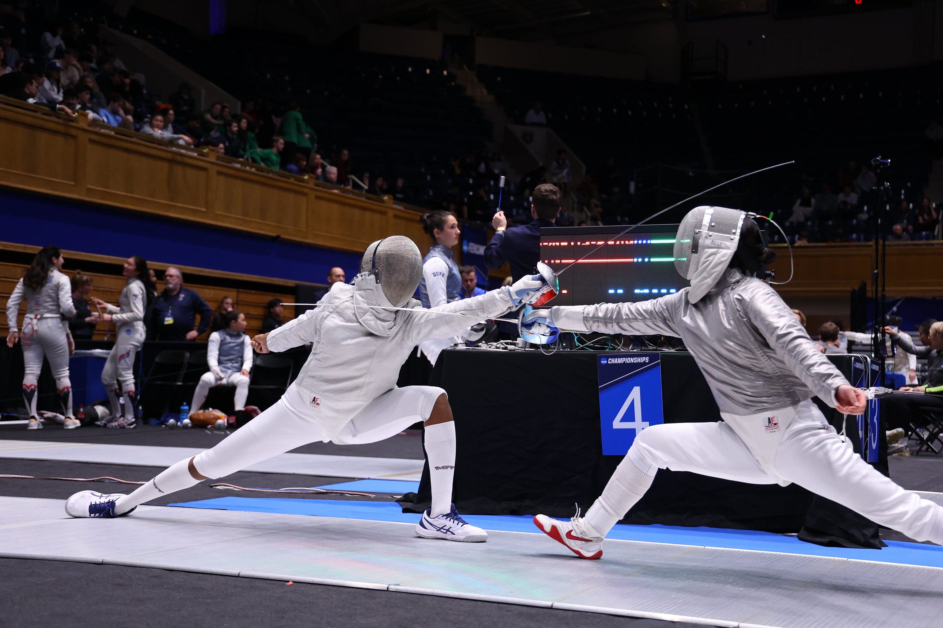 A photo of MIT alum Kristen Palmer at an indoor fencing competition in a fencing suit facing an opponent