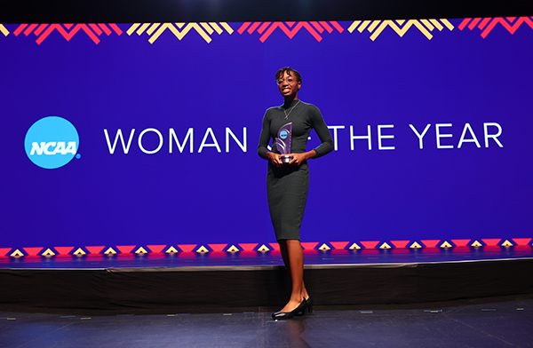 A photo of MIT alum Kristen Palmer standing on a stage in front of an electronic screen that says "woman of the year"