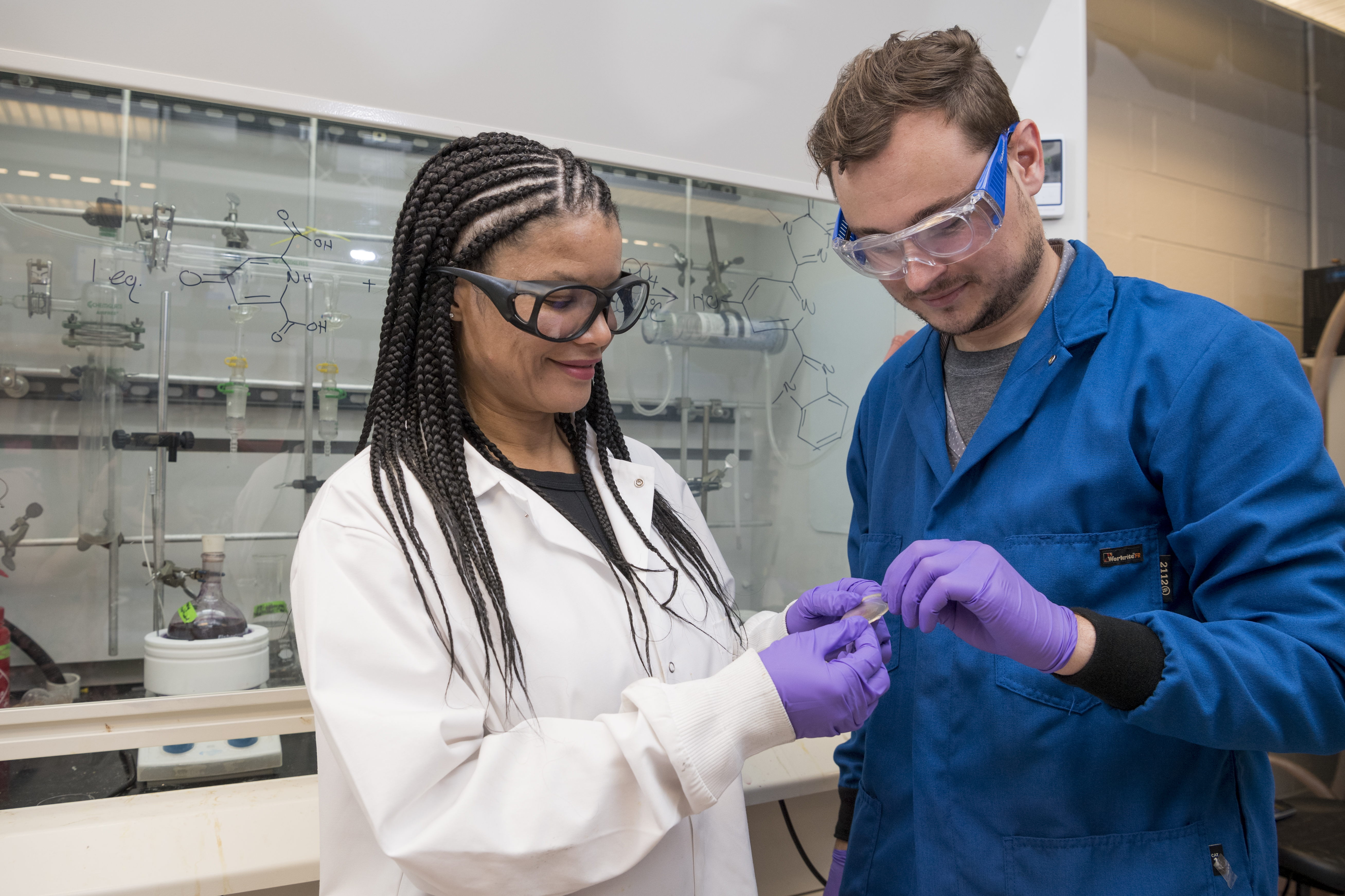 Woman in lab with gloves and lab coat holding object with man in lab 