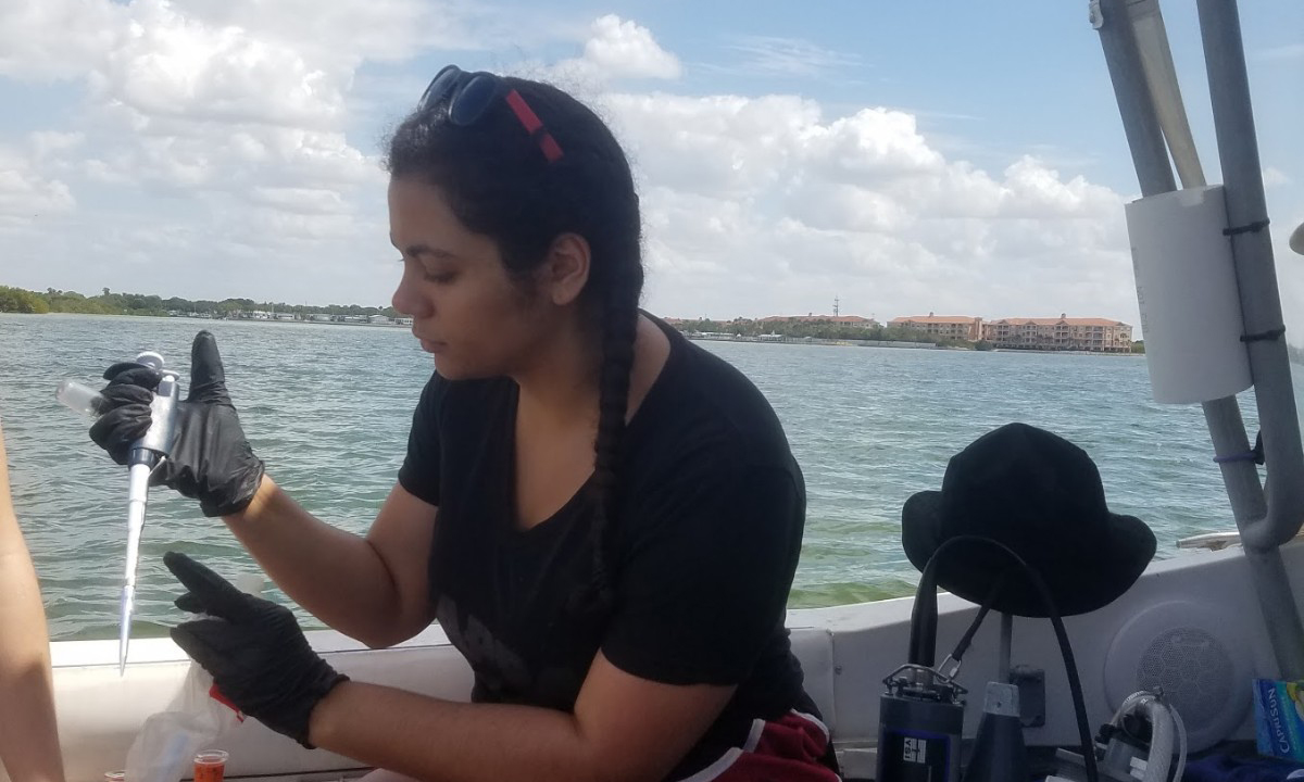 Elise Myers, in a boat on the open water, takes a water sample