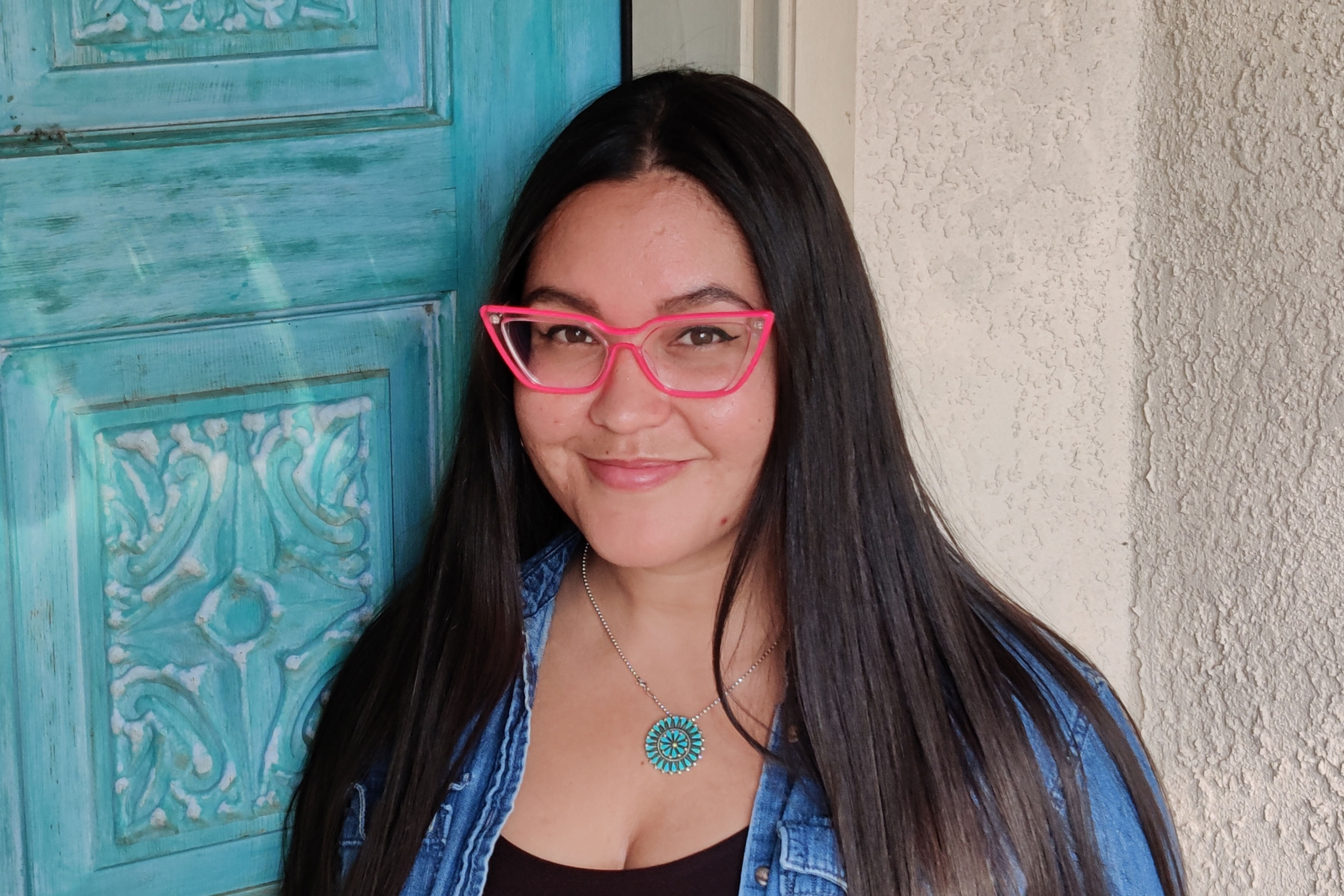 Photo of Jenny Lacika standing in front of a wall with a blue door on her left 