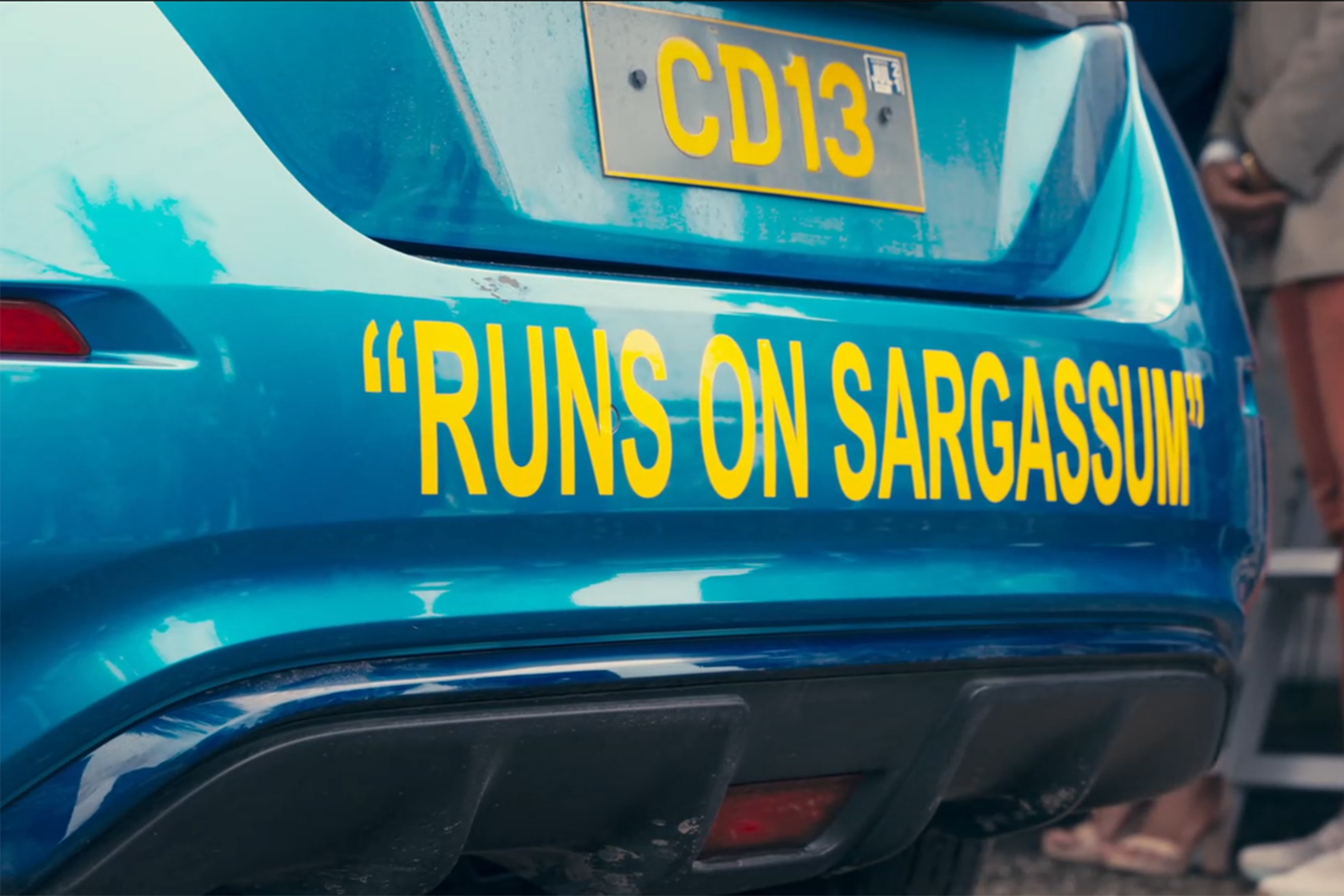 A photo of a blue car's bumper with the words "runs on sargassum" on it 