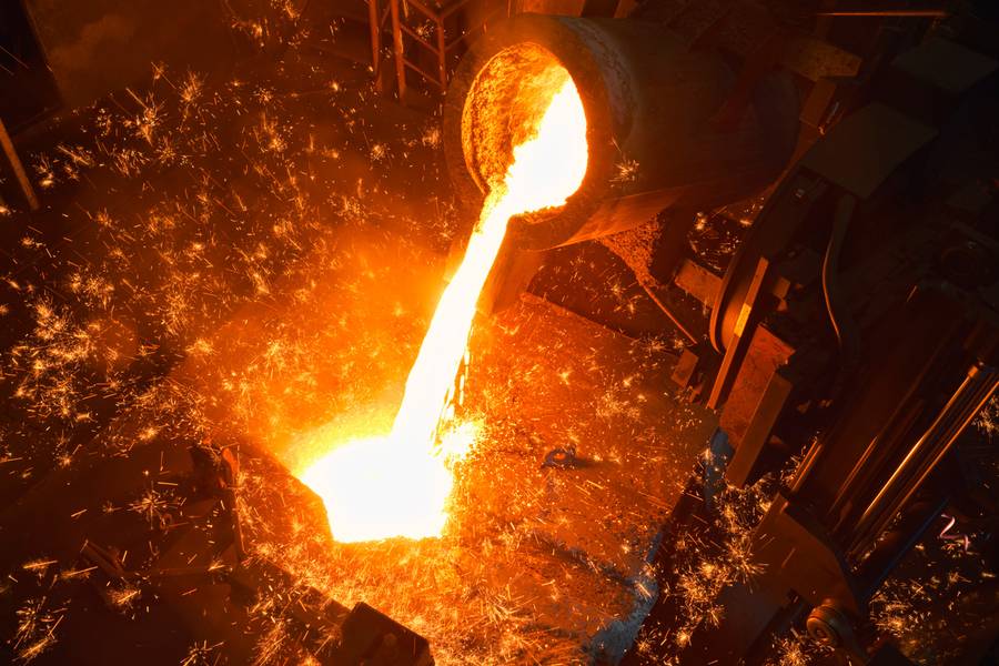 White-hot steel is shown being poured from a pipe into a receptacle. Sparks fly.