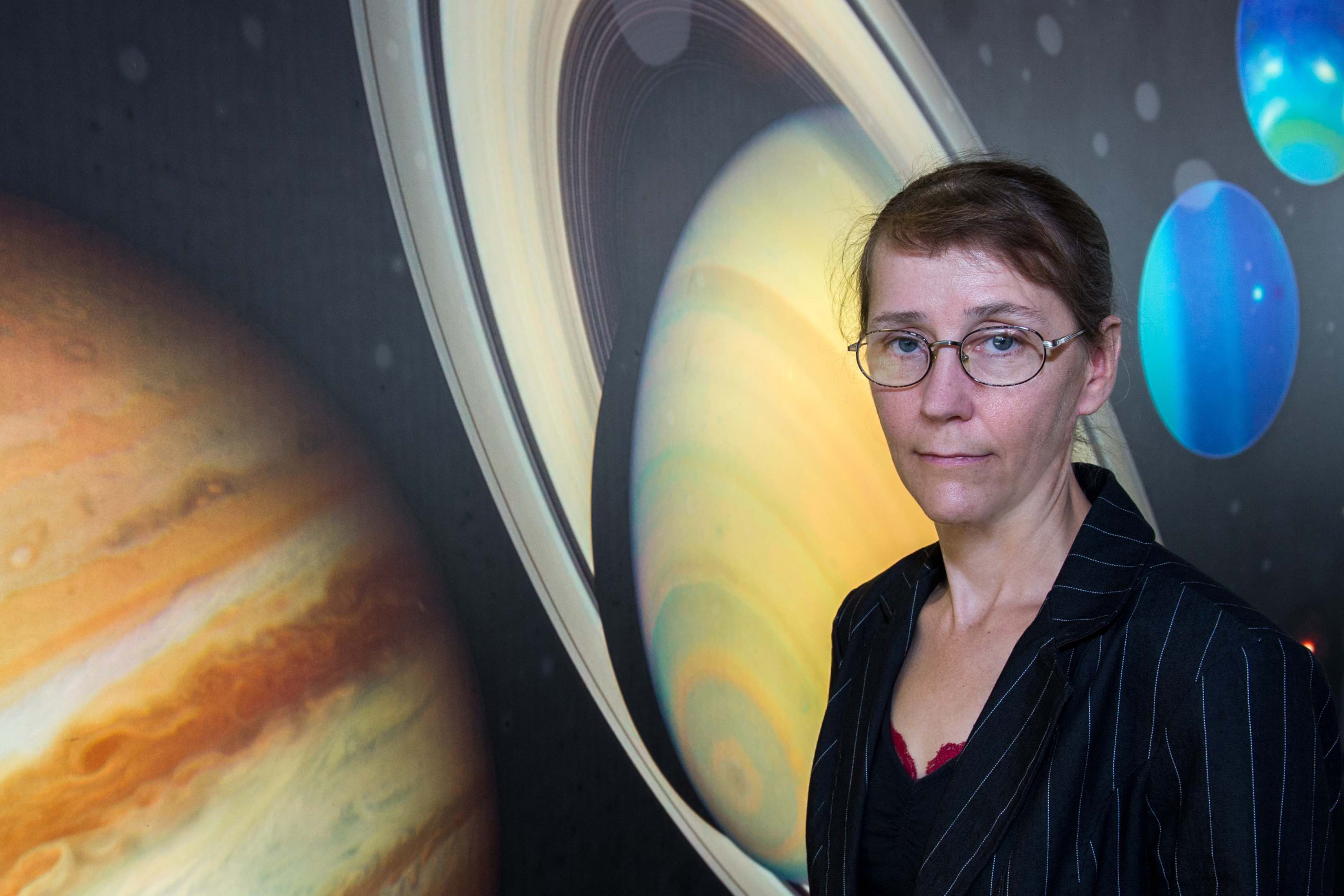 Catharine Conley poses in front of images of Neptune and Saturn.