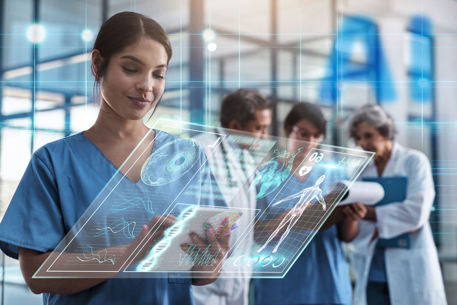 A person in blue scrubs appears to consult a screen of information displayed in midair. Other apparent medical professionals can be seen in the background.