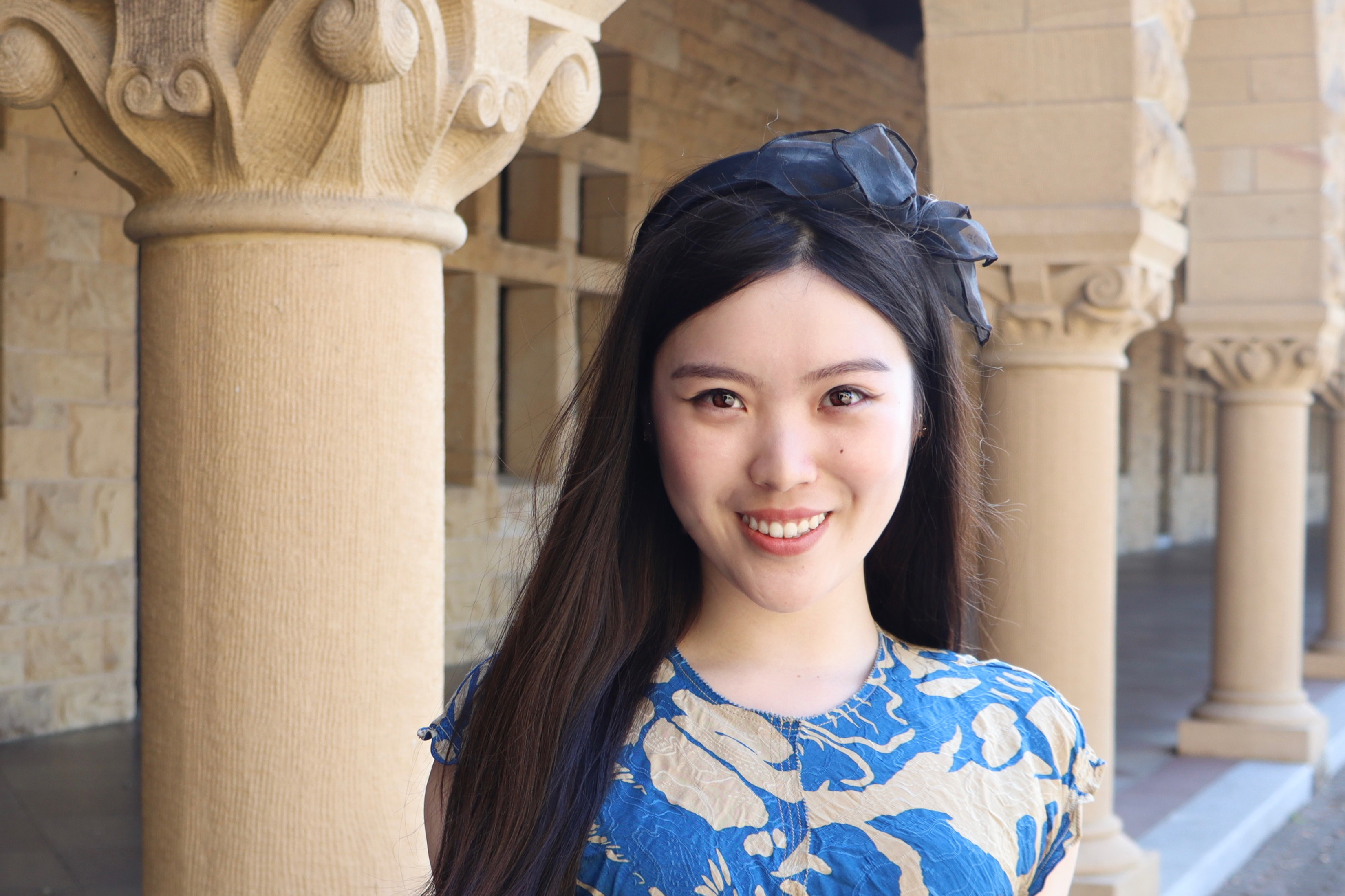 Portrait of Carina Hong with ribbon in her hair and columns in the background. 