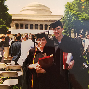 A photo of Yevgeniya Nusinovich and Aaron Ucko wearing a graduation cap and gown standing in front of the MIT great dome