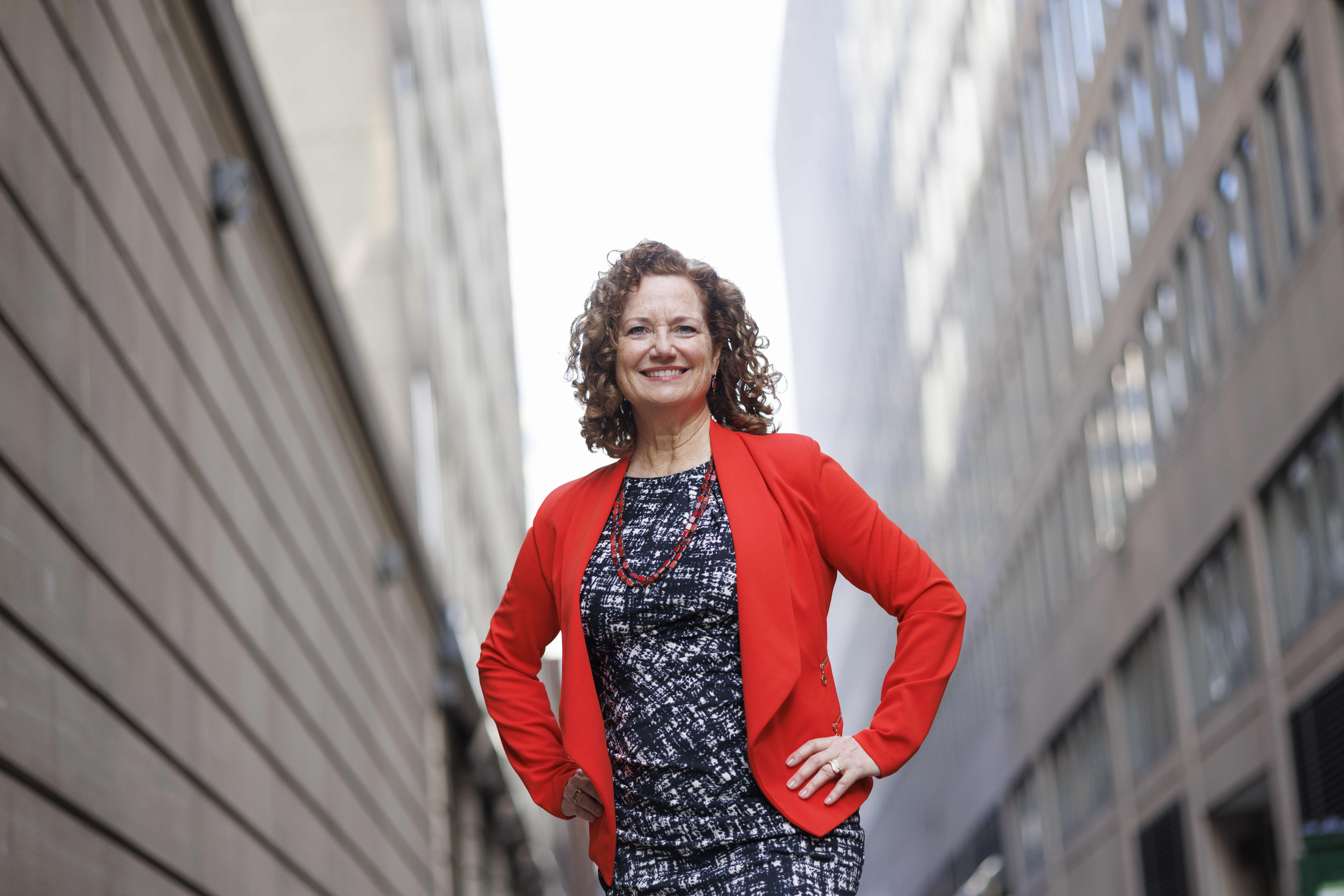 A photo of MIT alum Natalie Lorenz Anderson standing outside with a building on either side of her with her hands on her hips