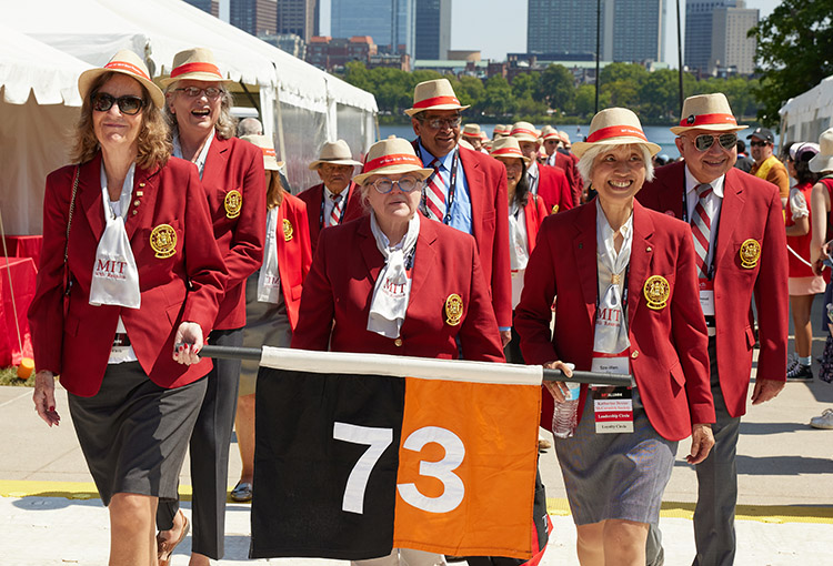 Alums in red jackets carry the orange and black '73 banner into Killian Court.