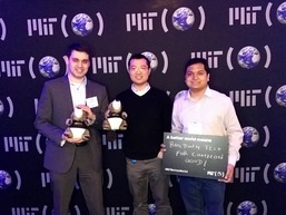 Three MIT alumni standing in front of background holding Tim the Beaver