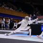 A photo of MIT alum Kristen Palmer at an indoor fencing competition in a fencing suit facing an opponent