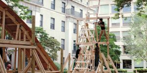 A photo of a wooden roller coaster structure outside in a courtyard with building surrounding it